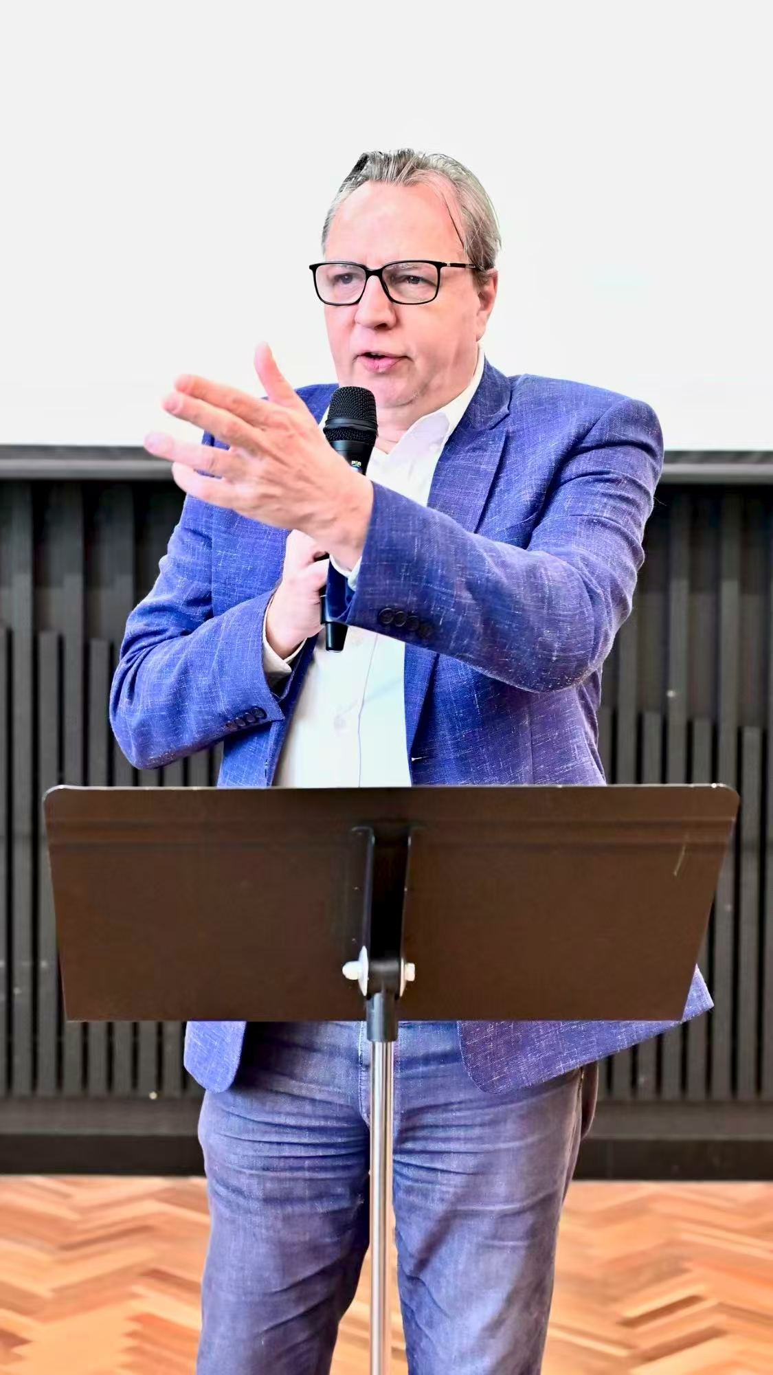 A speaker wearing a blue suit addressing the gathering at the lectern