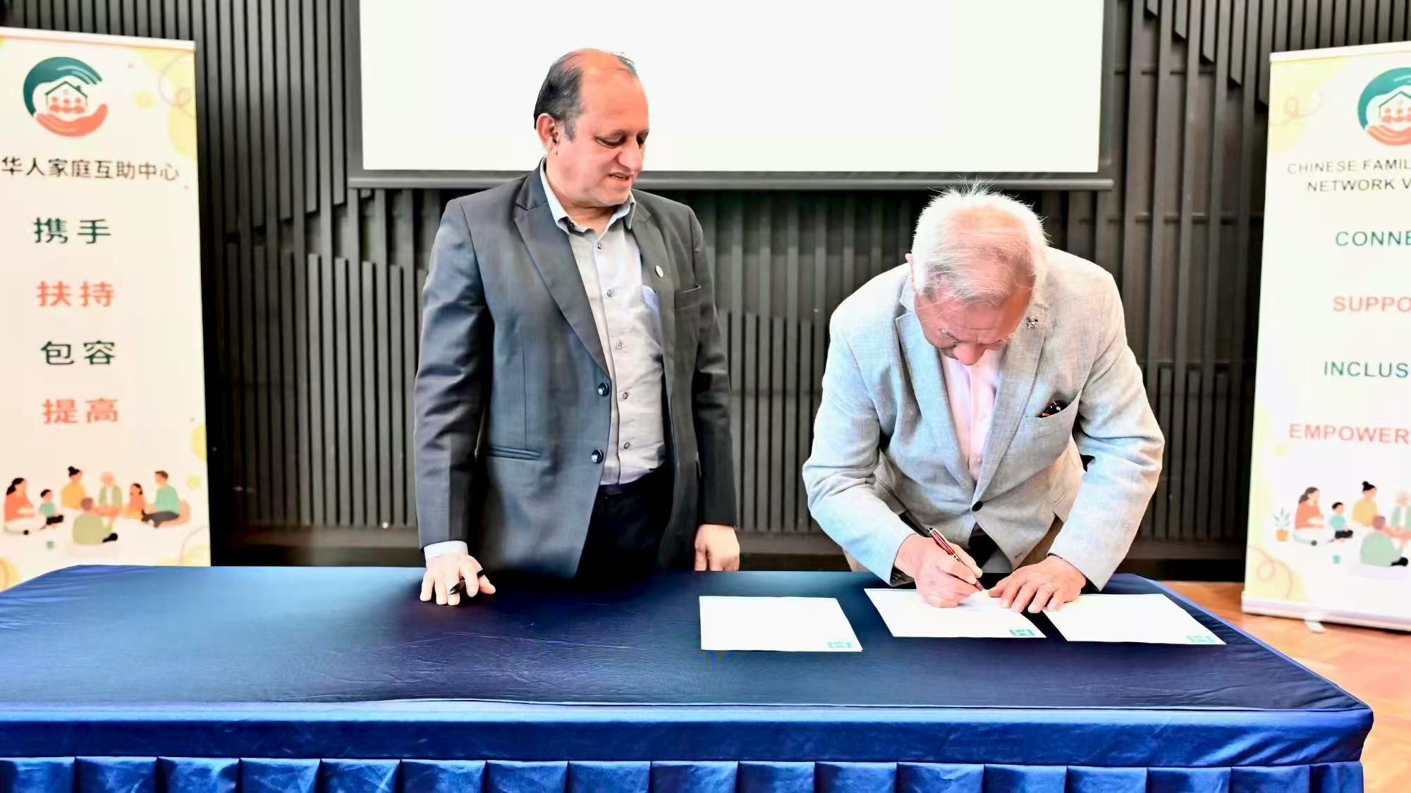 Two representatives signing partnership documents at a table during the event