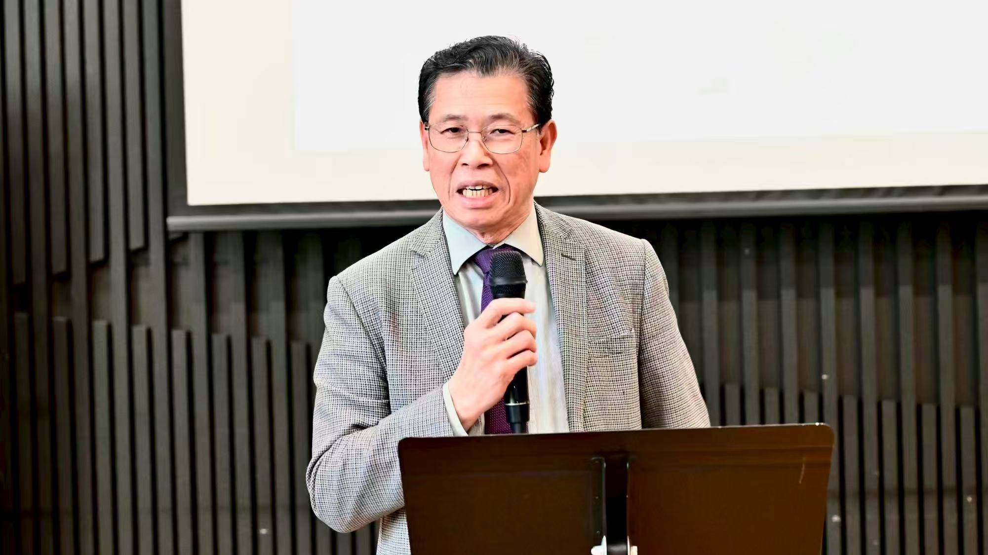A speaker in a checked suit speaking into a handheld microphone