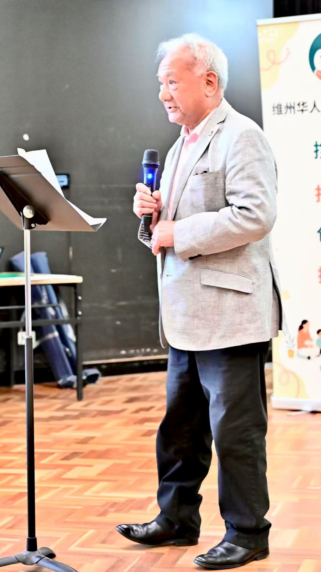 A speaker in a light grey suit addressing the gathering at the lectern