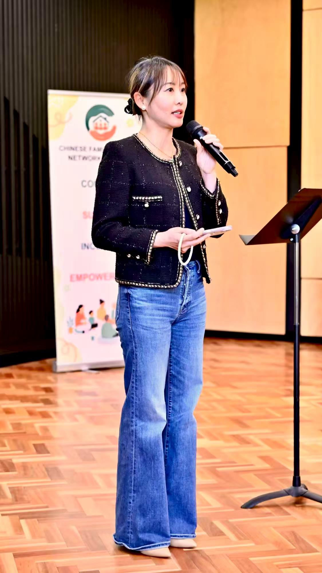A speaker in a dark jacket holding a microphone while speaking