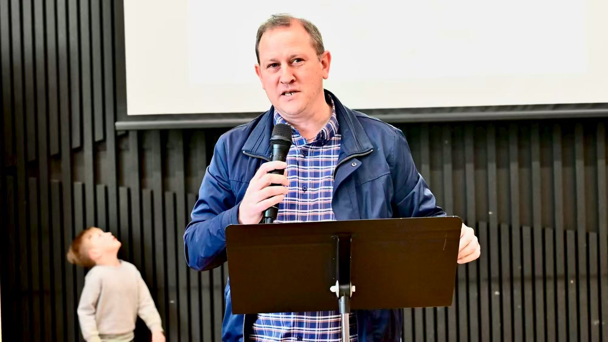 A speaker in a blue jacket speaking at the lectern
