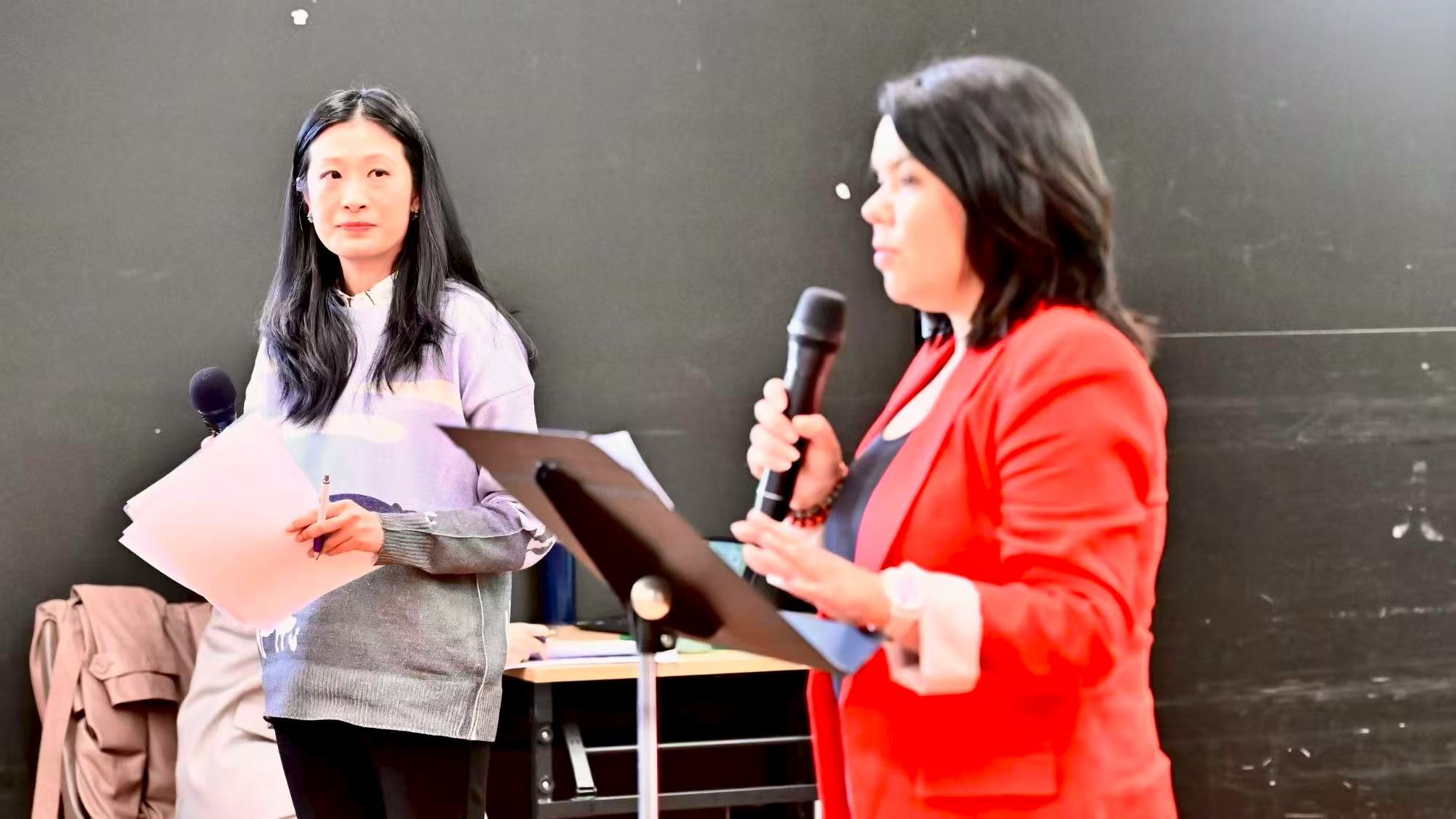 Two speakers holding microphones and notes while addressing the gathering