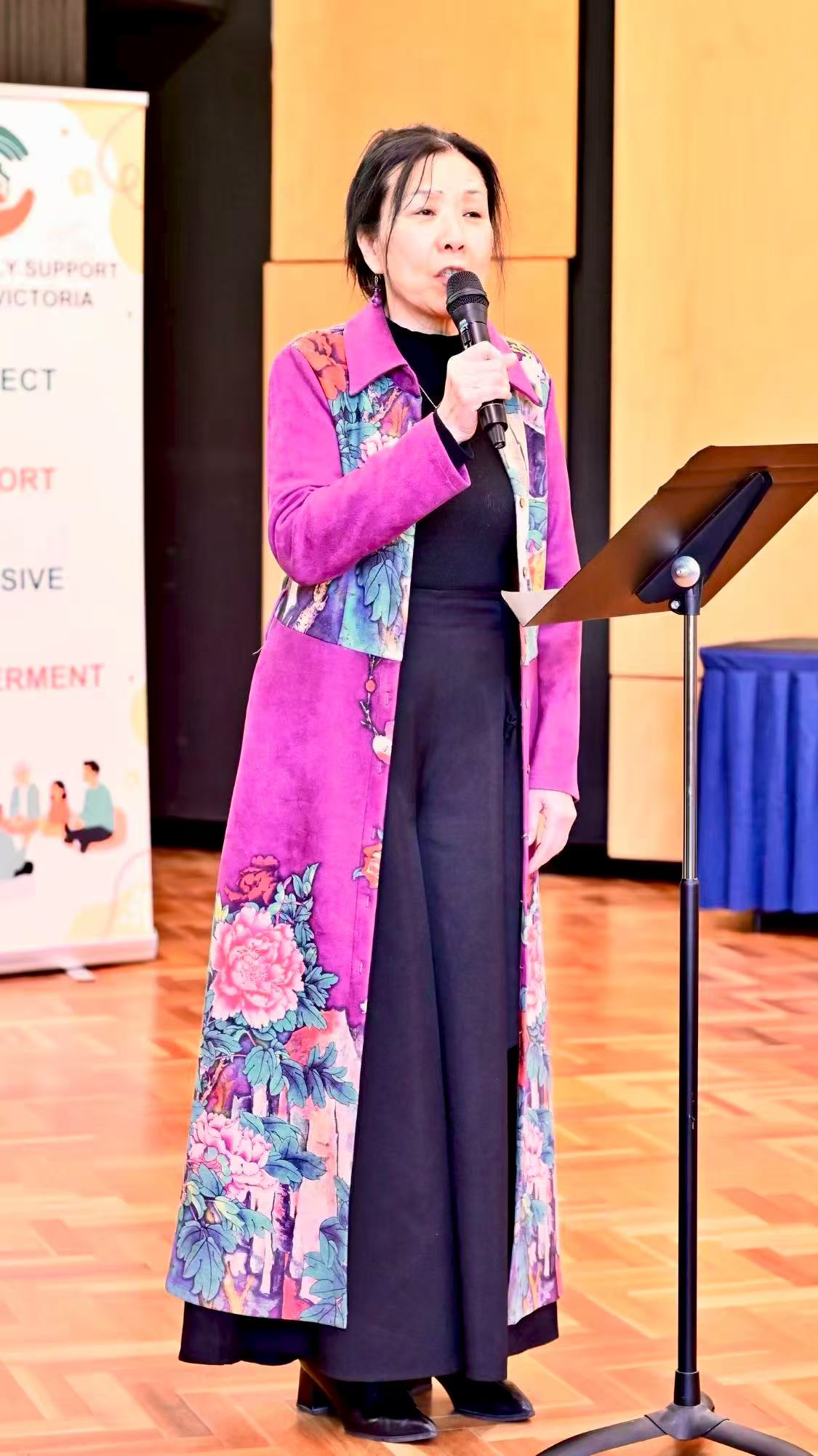 A speaker wearing a purple jacket addressing the gathering