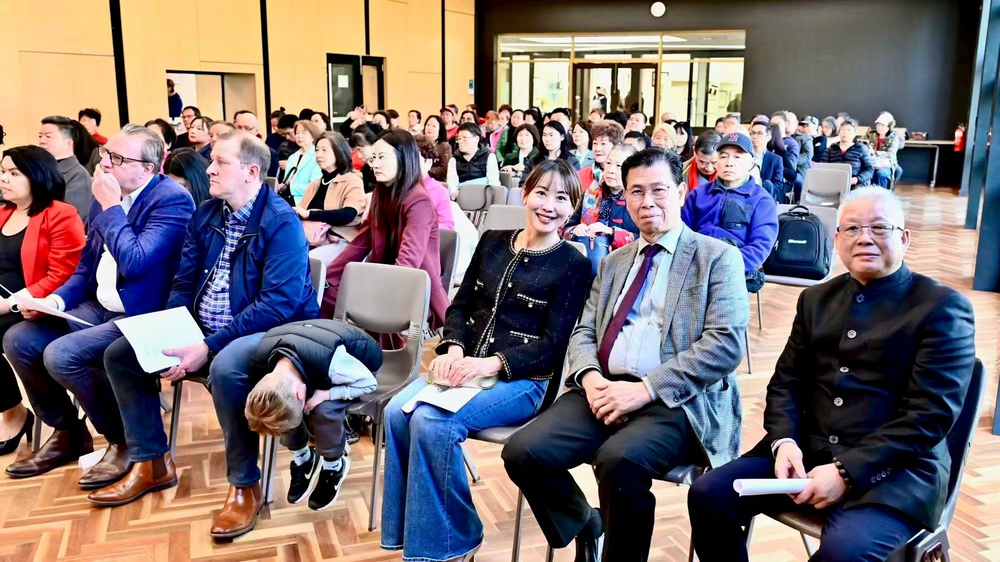 Front-row guests posing for a photograph with other attendees seated behind them